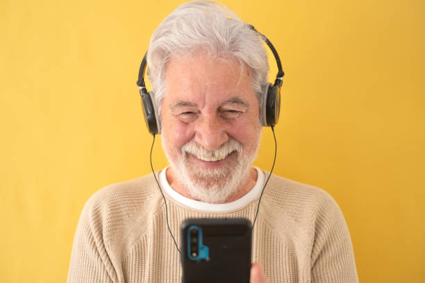 istock Happy senior white-haired man wearing headphones while using mobile phone. Elderly grandfather enjoying tech and social 1368238315