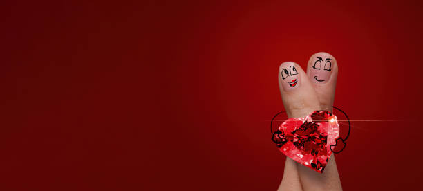 the happy finger couple in love with painted smiley and hold diamond ring heart shape on red background. stock photo
