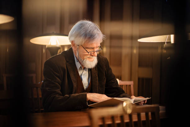 istock Senior man reading a book in the library 1368244465