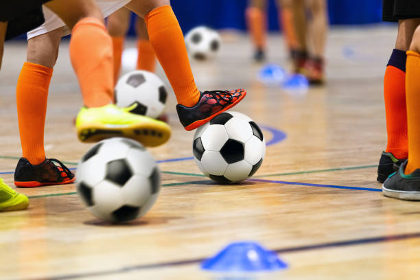 corso di calcio indoor per bambini presso il palazzetto dello sport della scuola. bambini che calciano palloni da calcio sul pavimento di futsal in legno. pratica sportiva di calcio per ragazzi in età prescolare - soccer child indoors little boys foto e immagini stock