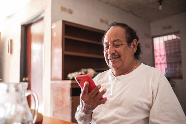 istock Latin senior man using the mobile phone at home 1368249677