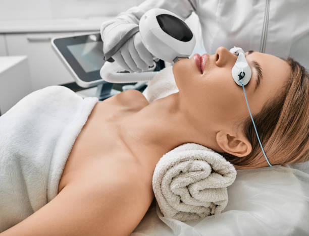 Photorejuvenation, rosacea treatment, removing brown spots and vascular mesh. Cosmetologist using IPL apparatus treats skin of female patient's face stock photo