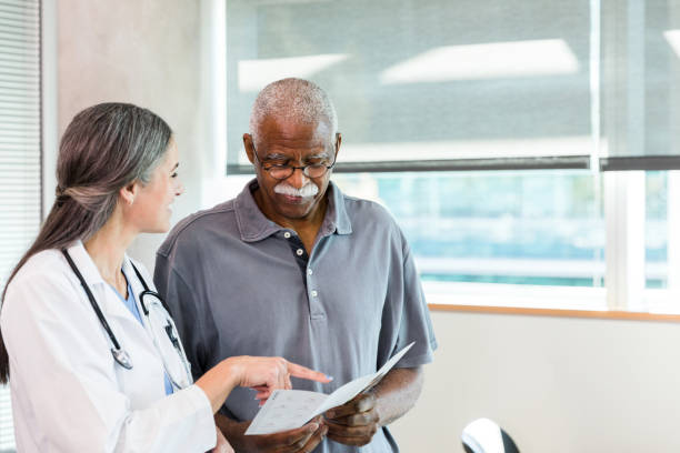l'uomo anziano guarda la brochure mentre il medico spiega le opzioni presentate - patient retirement senior adult hospital foto e immagini stock