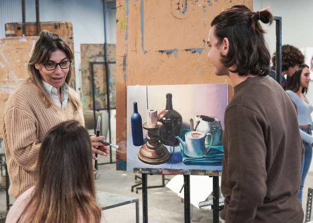 istock Mature female teacher working with students doing creative art painting inside classroom at university 1368252375