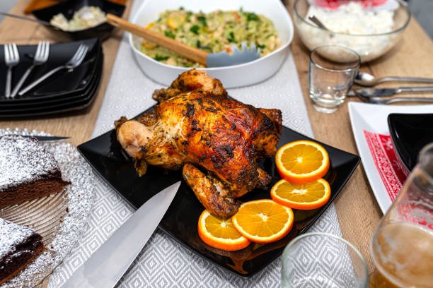 食べ物で満たされたテーブルの上に黒い皿の上に横たわっているクリスピーな皮を持つロースト全体の鶏肉。 - rotisserie ストックフォトと画像