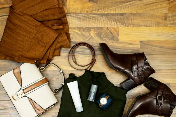 A set of fashionable clothes and accessories. green sweater and corrugated skirt, handbag, ankle boots and brown leather belt and tube face cream, nail polish on wooden table, Flat lay. Be in trend