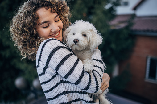 Portrait of a curly young woman holding her pet dog outdoors.