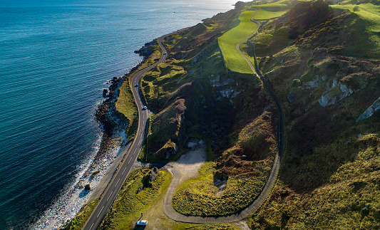 Northern Ireland. Atlantic coastline with famous coast road called Causeway Coastal Route and cliffs. One of the most scenic coastal roads in Europe. Aerial view in winter with cars against the sun