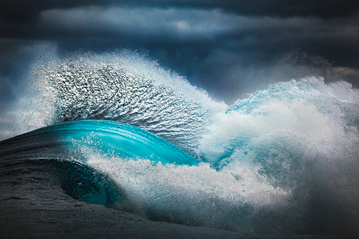 Close up detail and textures of vibrant blue ocean waves colliding in front of dark grey sky