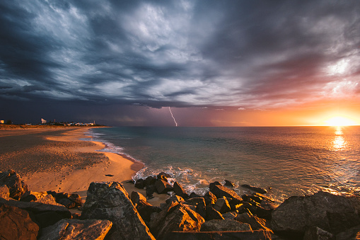 Incredible beach sunset during lightning storm beneath dark dramatic clouds