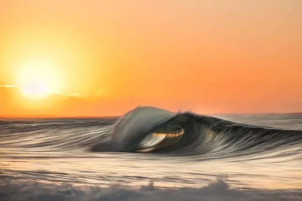 Photo of Perfect ocean wave breaking in front of beautiful sunrise