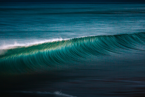 Perfect teal blue ocean wave cresting out at sea