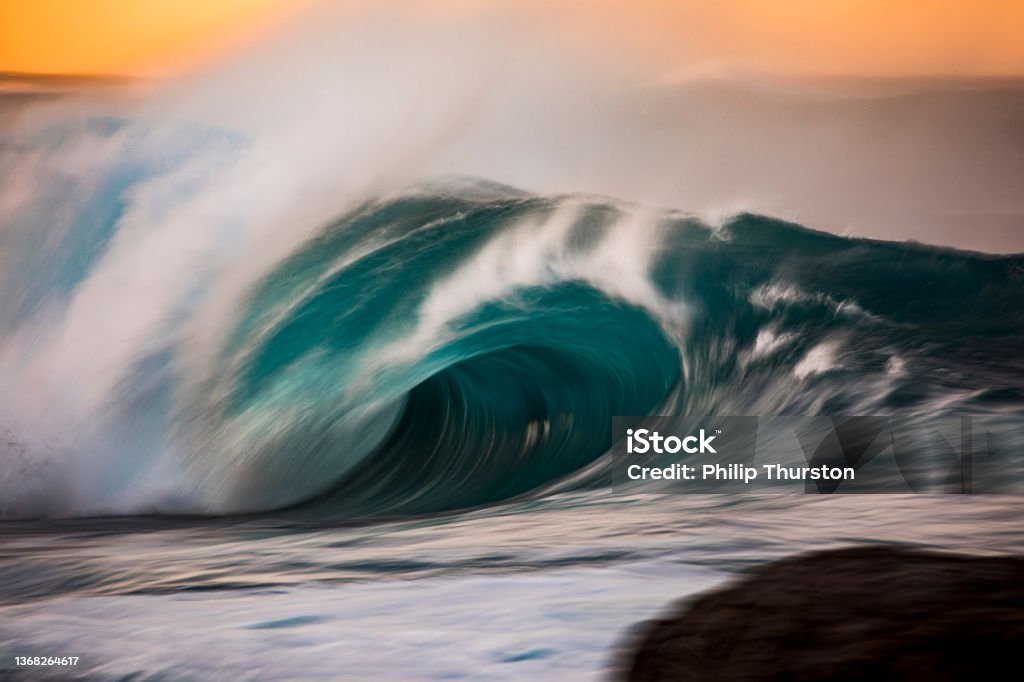 Powerful crashing turquoise wave in front of golden sky Teal Stock Photo