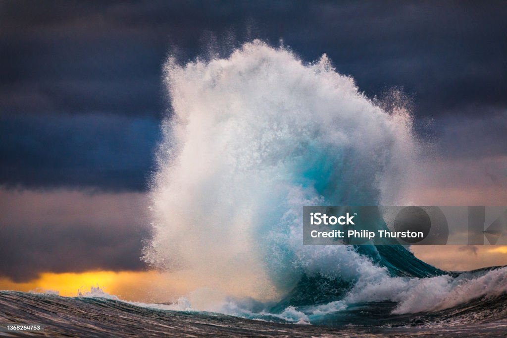 Powerful wave exploding into sky during multi colored sunset Powerful blue wave exploding into sky during multi colored sunset Wave - Water Stock Photo