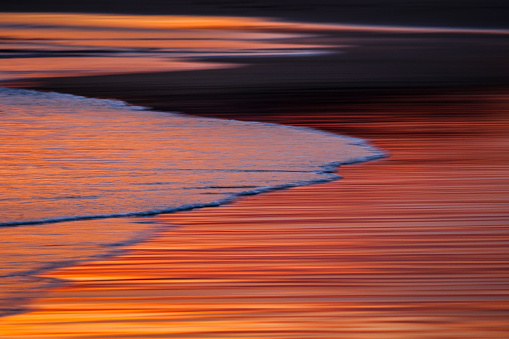 Slow shutter of ocean gliding onto shore during multi colored vibrant sunset