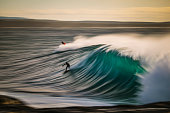 istock Slow shutter of surfers riding perfect teal blue wave 1368265422