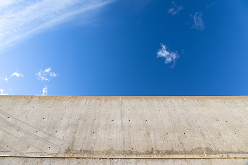 Gray cast concrete bridge structure seen from below, blue sky with clouds, creative copy space, horizontal aspect