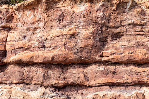 Rocky cliff face showing striations between the different layers of colored rocks, nature backdrop, horizontal aspect