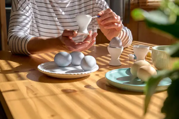 Woman preparing colored easter eggs and painting eggcup for Easter holiday celebration.