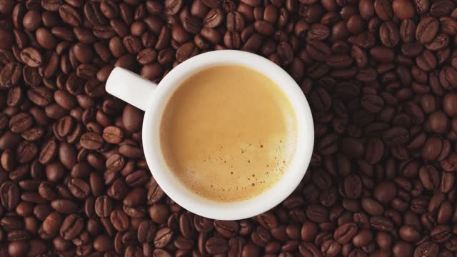 Cup of fresh aromatic coffee with crema, rotate with coffee beans, top view.