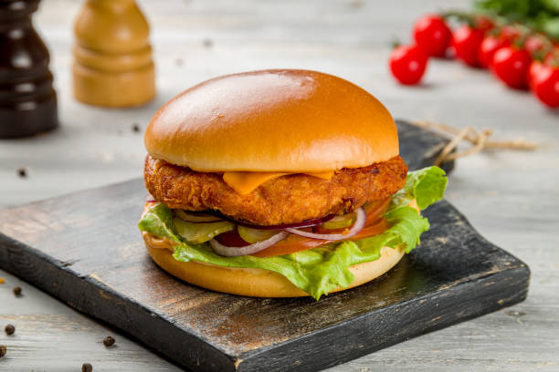 Burger with chicken, tomato, red onion and greens with sauce on the board