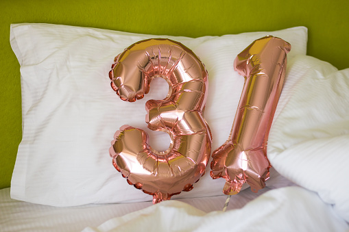 Pink foil balloon number in bed. Festive surprise, birthday present. Birthday greeting card with inscription 31.