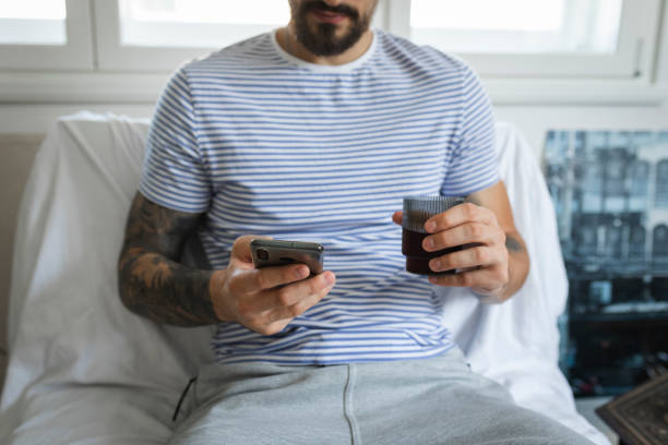istock Casual Anonymous Young Man Using His Smartphone at Home while Sitting Down and Having a Drink 1368276695