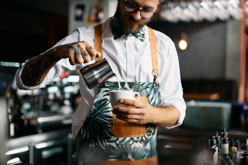 Close-up of barista making coffee and adding milk while working in a bar.