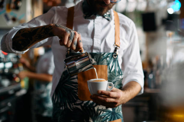 istock Close-up of barista making cappuccino and adding milk while working in a bar. 1368278220