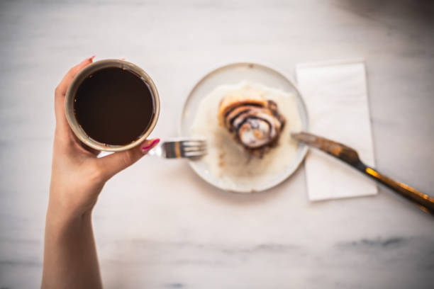 Woman drinking coffee and eating cinnamon roll ( close up )