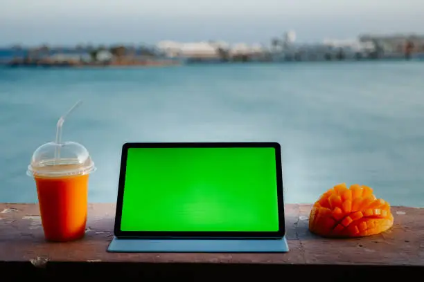 Tablet with green screen on balcony with seaview. Work while traveling