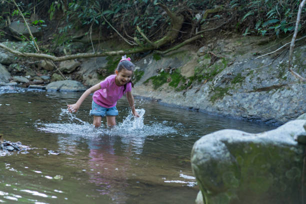 7-year-old Latin girl casually dressed from Colombia Bogota is inside the river that passes near her farm having fun with the water surrounded by natural stones