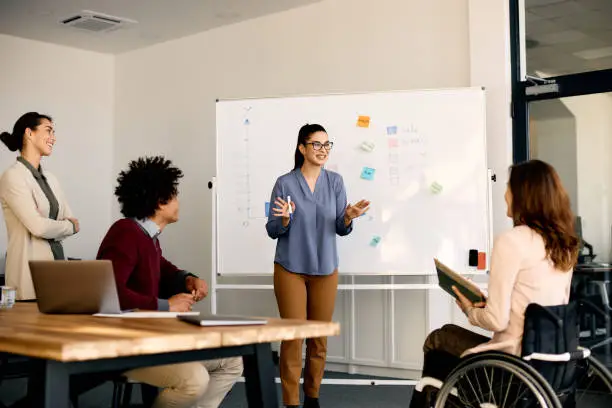 Photo of Young happy businesswoman giving presentation to group of her colleagues in meeting room.