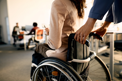 Close-up of disabled businesswoman pushing her disabled coworker in wheelchair at corporate office.