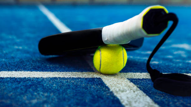 pelota amarilla por la raqueta en el suelo detrás de la red de pádel en cancha azul al aire libre. - tennis court tennis net indoors fotografías e imágenes de stock