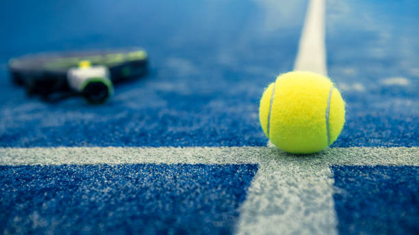 palla gialla sul pavimento dietro la rete da paddle nel campo blu all'aperto. padel tennis - padel foto e immagini stock
