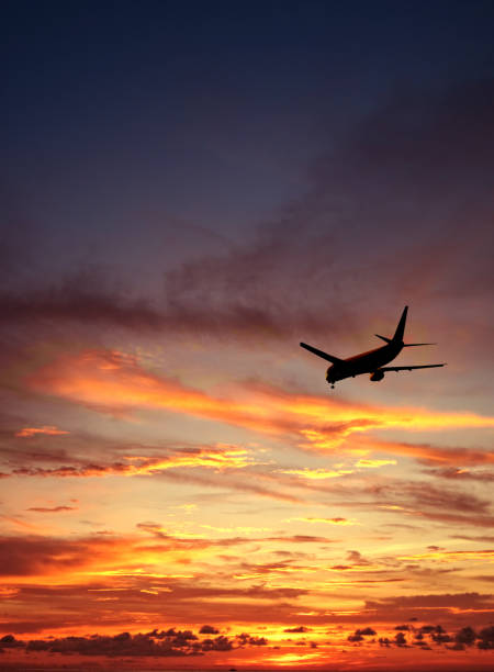 Flying commercial airplane over orange color dramatic sunset sky Transportation image of flying commercial passenger airplane over sunset sky wow airlines stock pictures, royalty-free photos & images