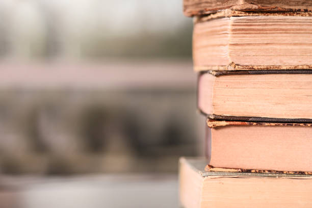 Stack of old, antique books on a table with a window defocused in background. No people.