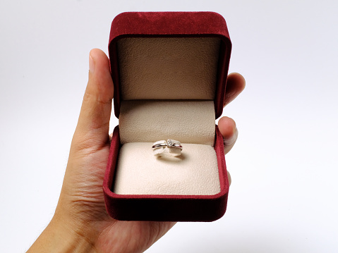 hands holding engagement ring and maroon gift box