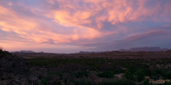 Panorama of a valley with the Chisos Mountains in Big Bend National Park at dusk with dramatic cloudscape.