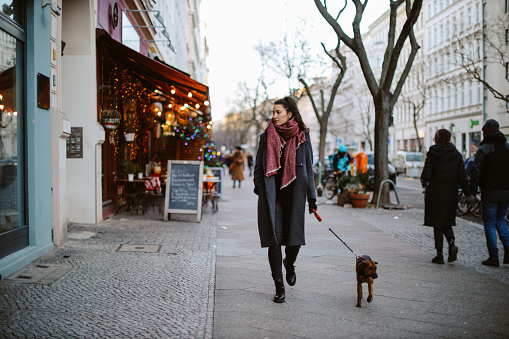 street style portrait of a young woman walking in Berlin Kreuzberg in winter with her pet dog.