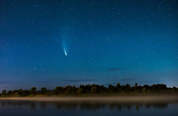 Photo of Comet in the night sky. Summer starry sky. Stars on sky. Beautiful night landscape. Long exposure. Conceptual photography. Fog over the water. Atmospheric landscape. Morning twilight. Comet Neowise