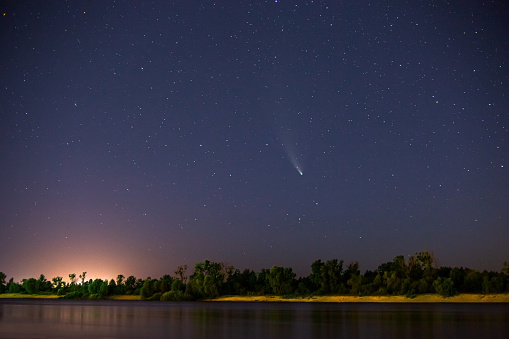 Comet in the night sky. Summer starry sky. Stars on the sky. Beautiful night landscape. Long exposure. Conceptual photography. Fog over the water. Atmospheric landscape.