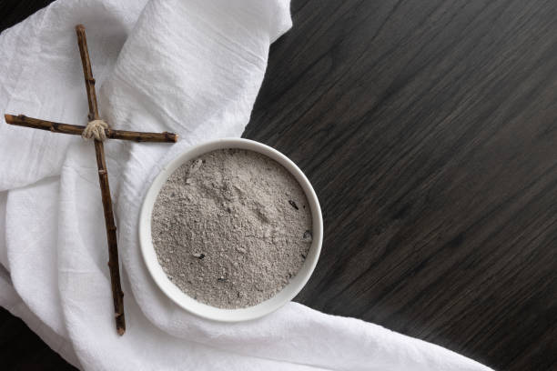 Cross, white linen and bowl of ashes on dark wood