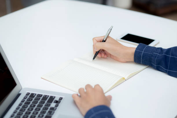 istock Closeup hand of business man writing on note while using laptop computer on desk at home, male planning on note for business success, author and blog, businessman working on table, employee and job. 1368309519