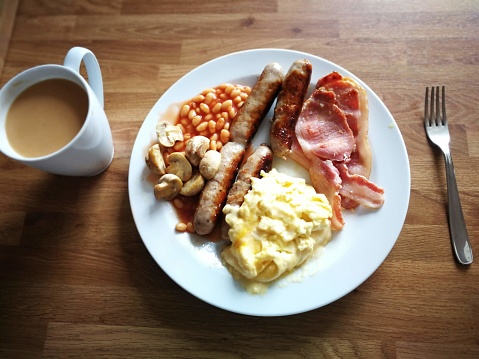 English breakfast with scrambled eggs, bacon, sausages,  mushrooms, baked beans, milk tea.