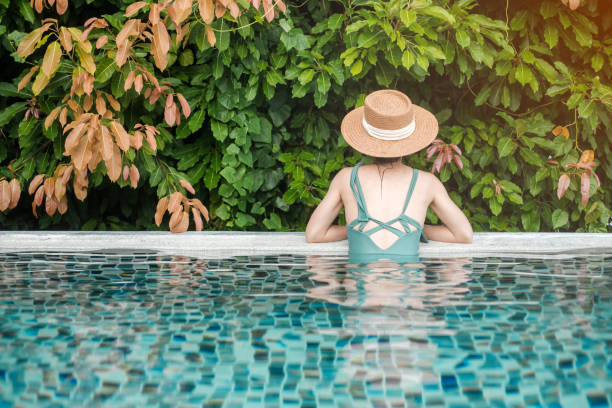 happy woman in green swimsuit and hat in swimming pool at luxury hotel against ocean front. young female enjoy in tropical resort. relaxing, summer,  travel, holiday, vacation and weekend concept - swimming pool resort swimming pool poolside sea imagens e fotografias de stock