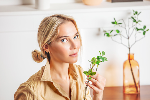 Portrait of a beautiful blonde woman with blue eyes with a green branch of a plant in her hand, close-up