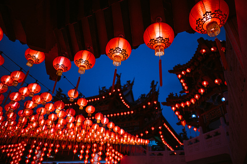 Round red lantern hanging on old traditional temple at night.