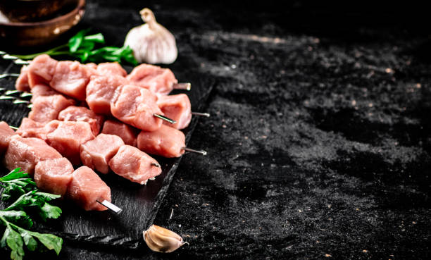 istock Pork kebab raw with greens and garlic on a stone board. 1368324536